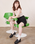 Hana is sitting in a vintage green and white chair wearing Trouser Shorts in Basic Black and a vintage off-white Tank Top