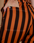 Close up of Alex's hand in back pocket of Black Stripe Work Pants in Construction Orange