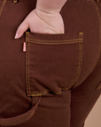 Close up of Ashley's hand in the back pocket of Carpenter Jeans in Fudgesicle Brown