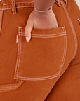 Carpenter Jeans in Burnt Terracotta back pocket close up. Meghna has her hand in the pocket.