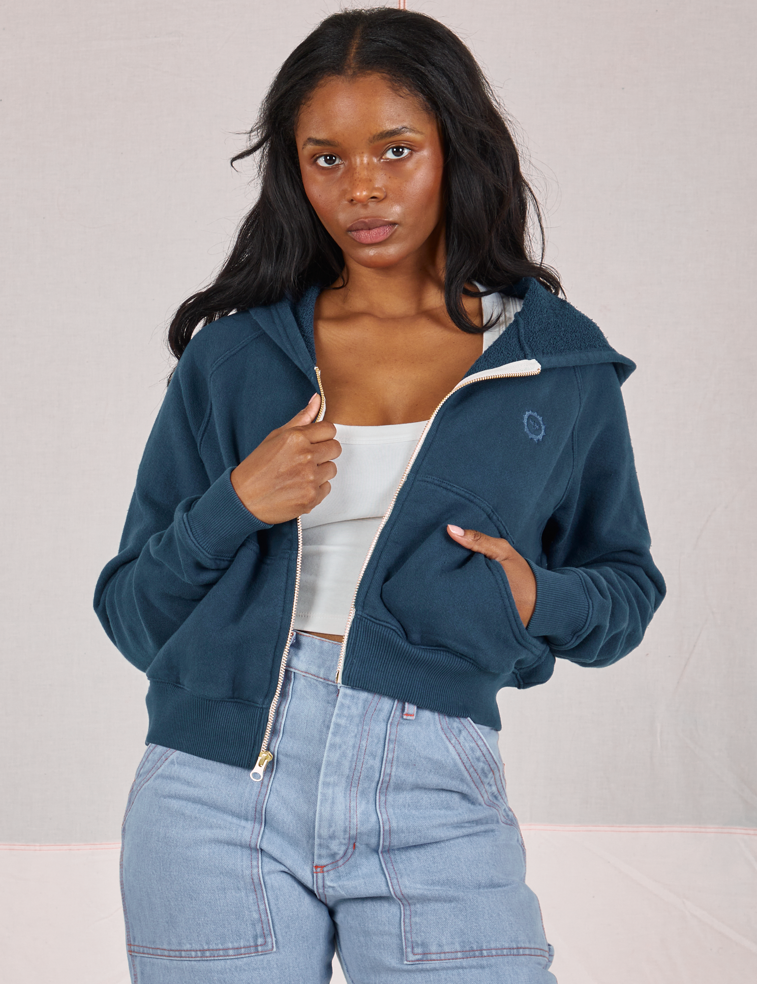 Kandia is wearing Cropped Zip Hoodie in Lagoon, a vintage off-white Cropped Tank underneath and light wash Carpenter Jeans