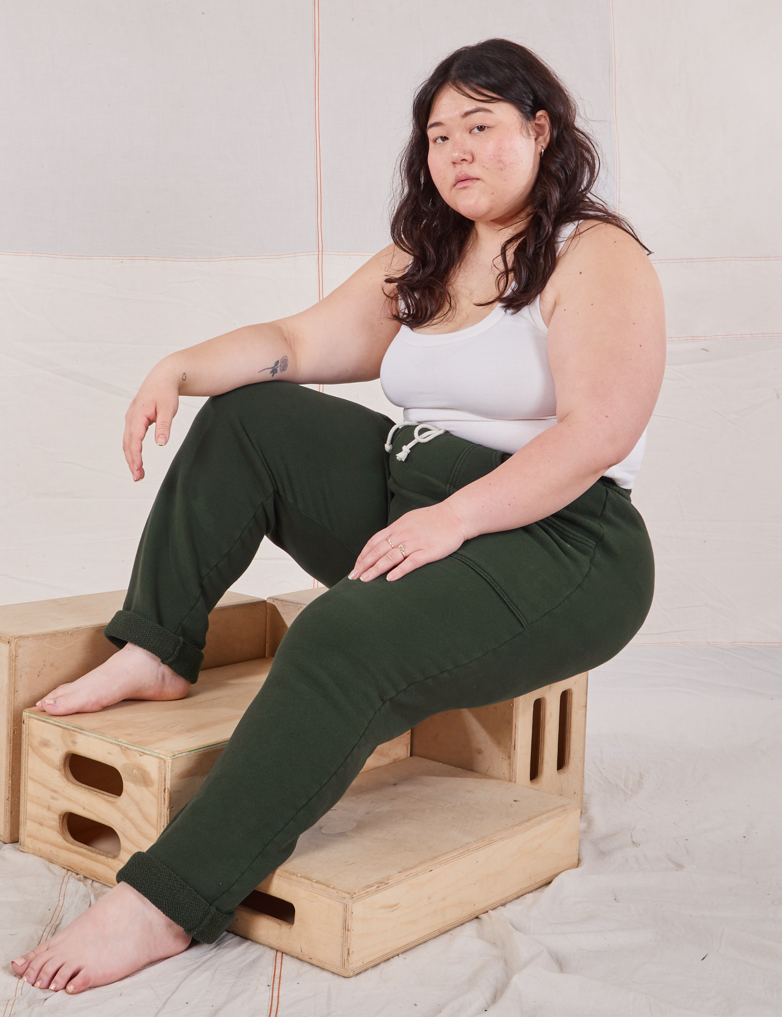 Ashley is wearing Rolled Cuff Sweat Pants in Swamp Green and vintage off-white Cropped Tank Top. She is sitting on a wooden crate.
