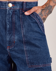 Carpenter Shorts in Dark Wash front pocket close up. Jesse has their hand in the pocket.