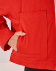 Close up of Anthony's hand in the front pocket of Mechanic Jacket in Mustang Red
