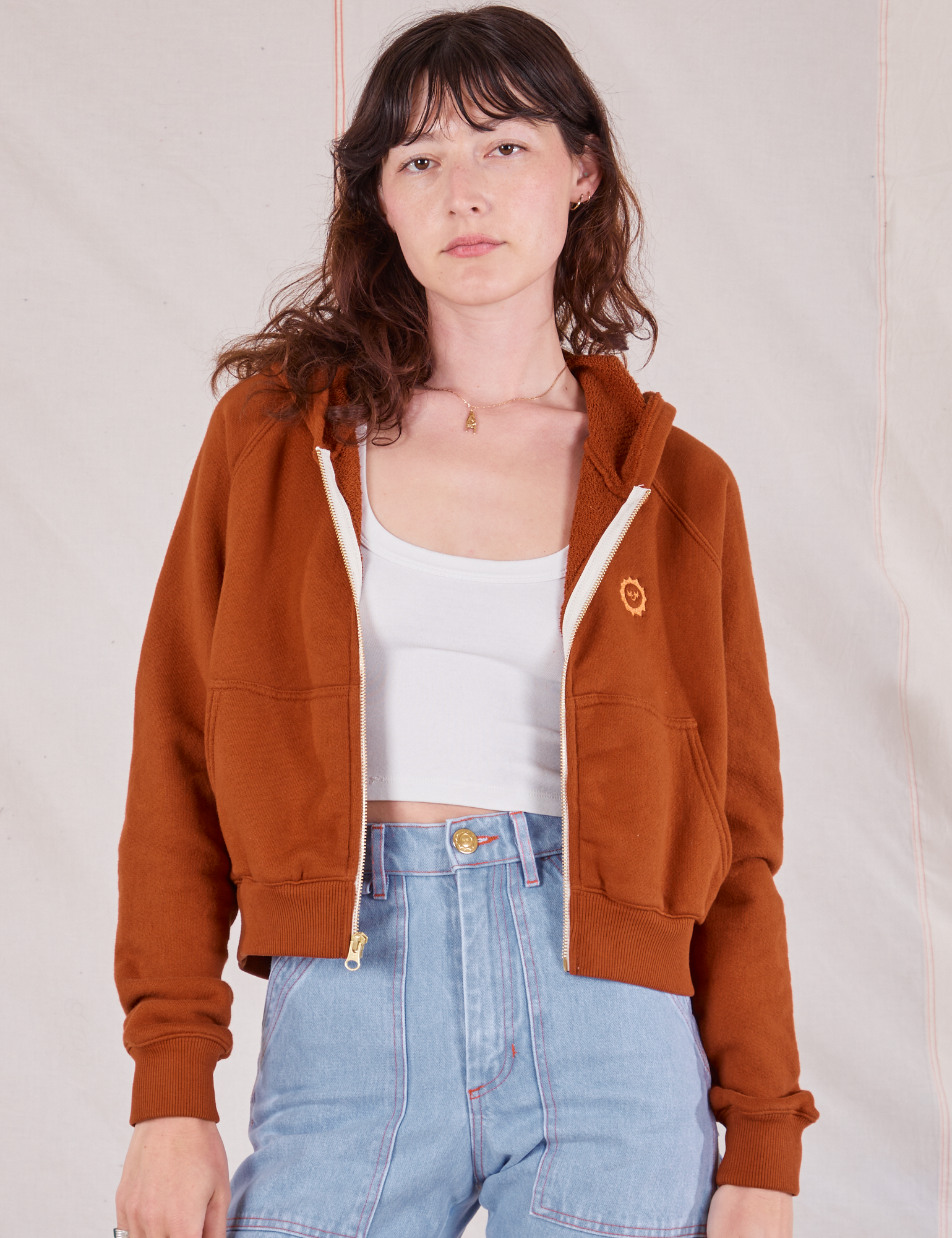 Alex is wearing Cropped Zip Hoodie in Burnt Terracotta, a vintage off-white Cropped tank and light wash Carpenter Jeans