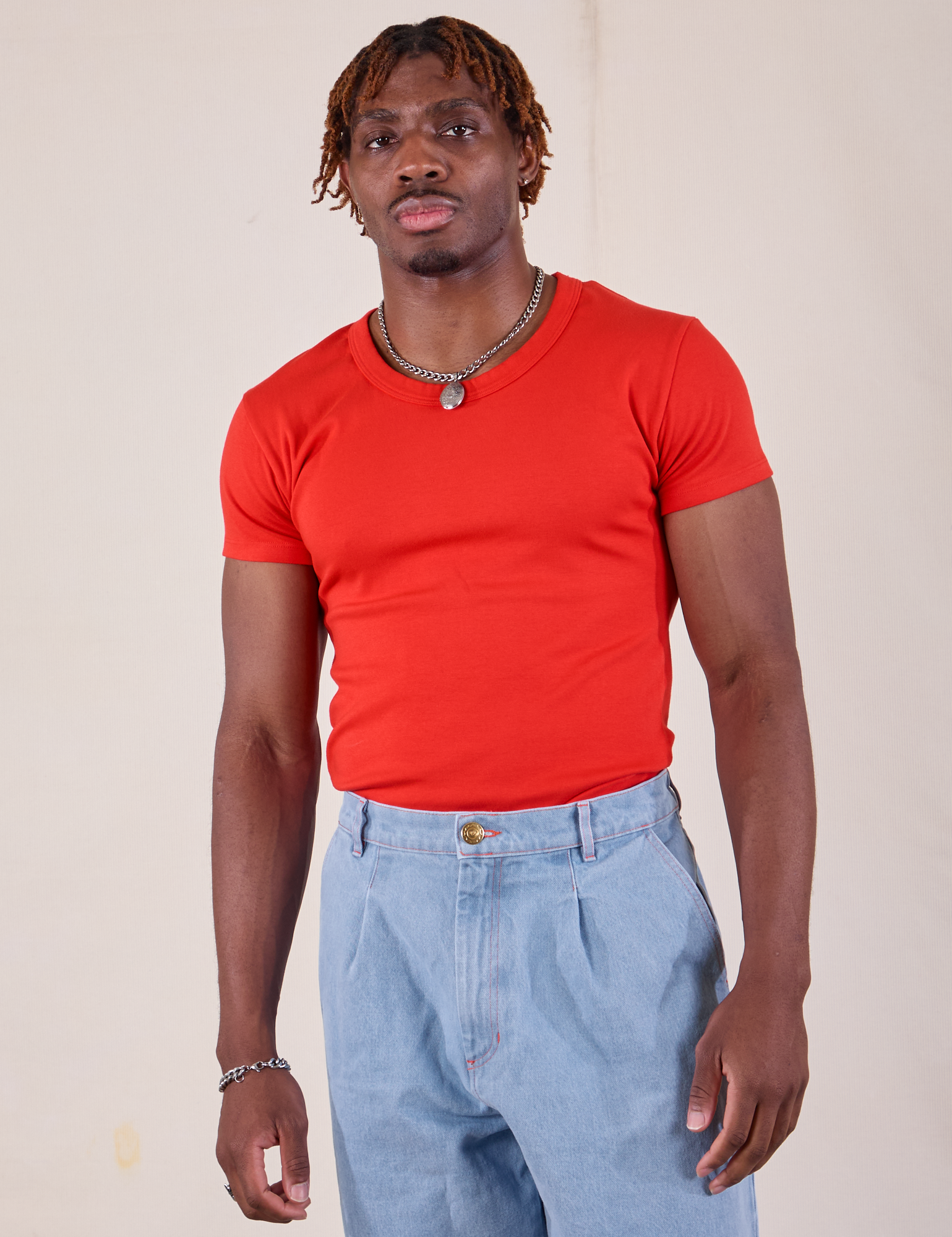 Isaac is wearing Baby Tee in Mustang Red tucked into light wash Denim Trousers