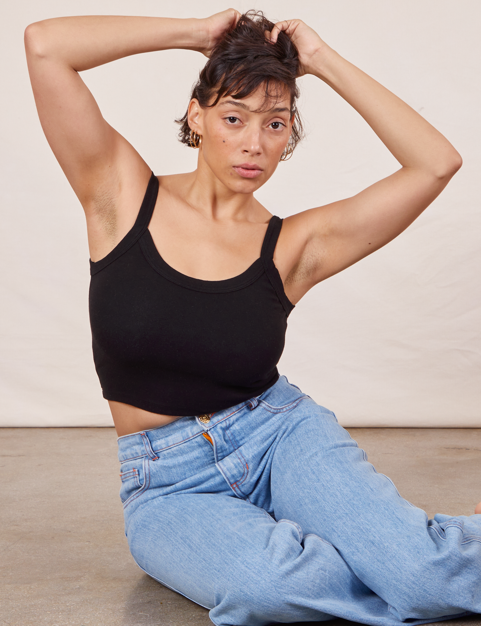 Tiara is sitting on the concrete floor wearing Cropped Cami in Basic Black and light wash Sailor Jeans