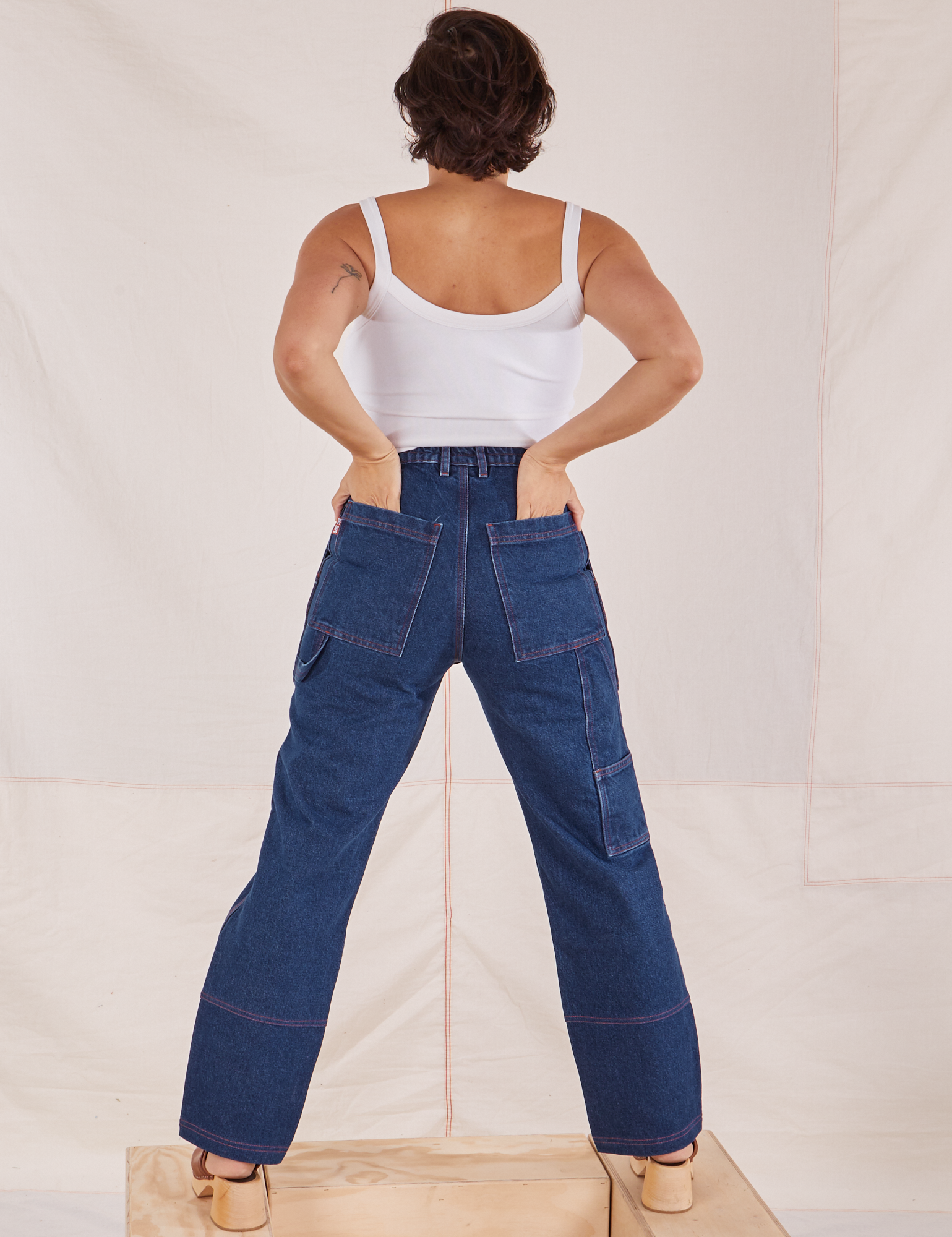 Back view of Carpenter Jeans in Dark Wash and Cropped Cami in vintage tee off-white Tiara has both hands in the back pocket.