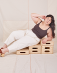 Ashley is lying across wooden crates wearing Heavyweight Trousers in Vintage Tee Off-White and espresso brown Cropped Cami.