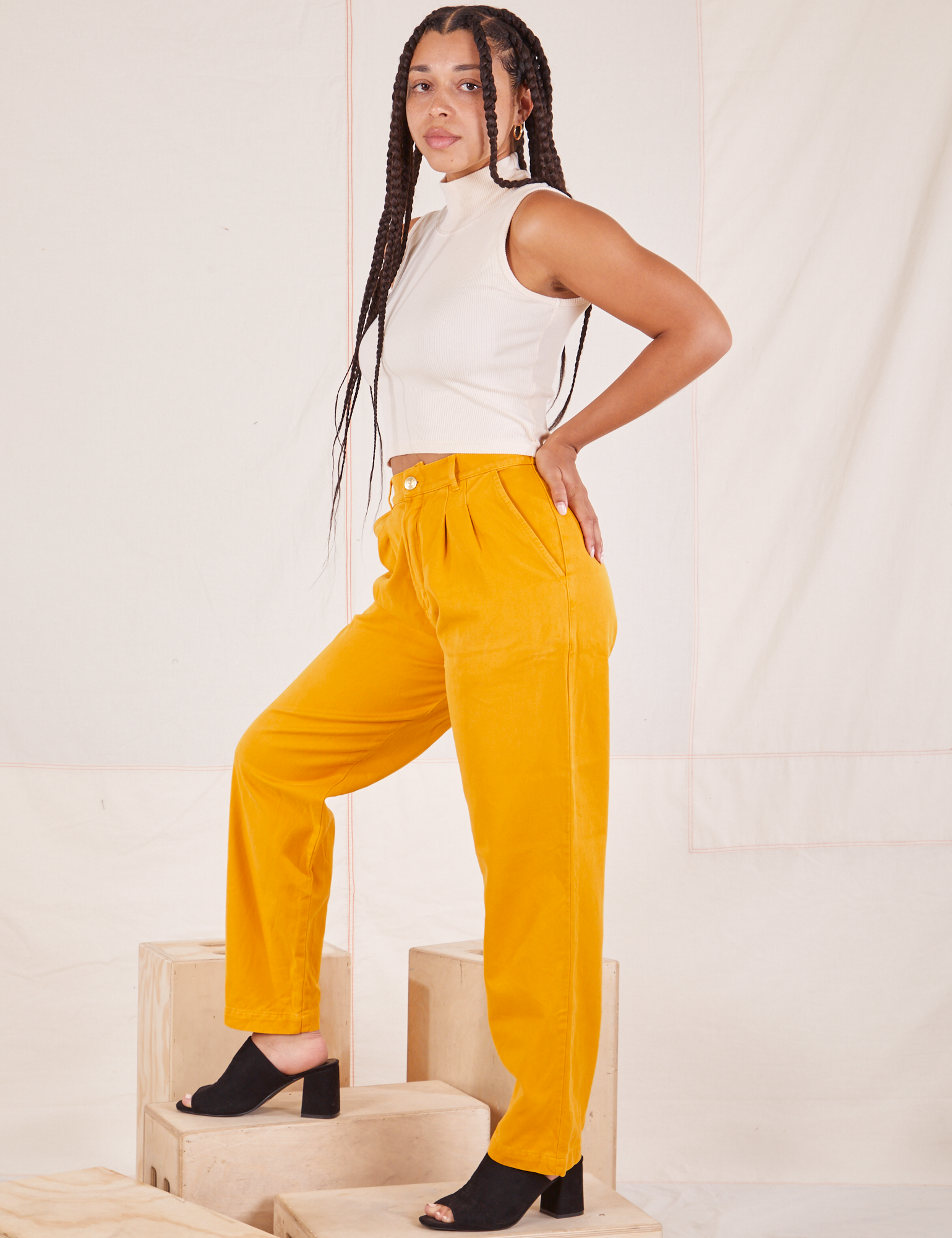 Side view of Organic Trousers in Mustard Yellow and Sleeveless Turtleneck in vintage in off-white worn by Gabi