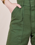 Front pocket close up of Petite Short Sleeve Jumpsuit in Dark Emerald Green. Hana has her hand in the pocket