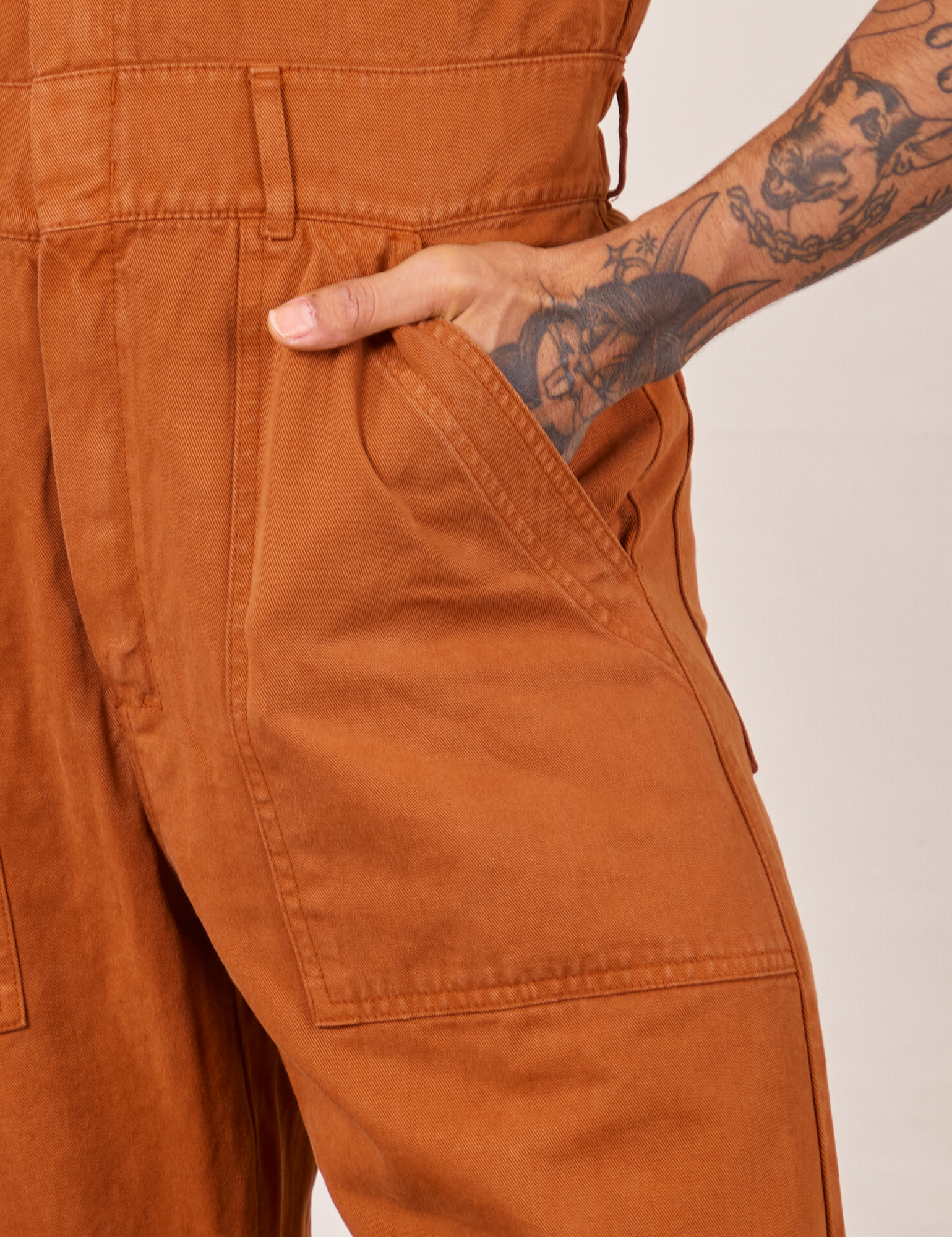 Front pocket close up of Short Sleeve Jumpsuit in Burnt Terracotta. Jesse has their hand in the pocket.