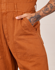 Front pocket close up of Short Sleeve Jumpsuit in Burnt Terracotta. Jesse has their hand in the pocket.