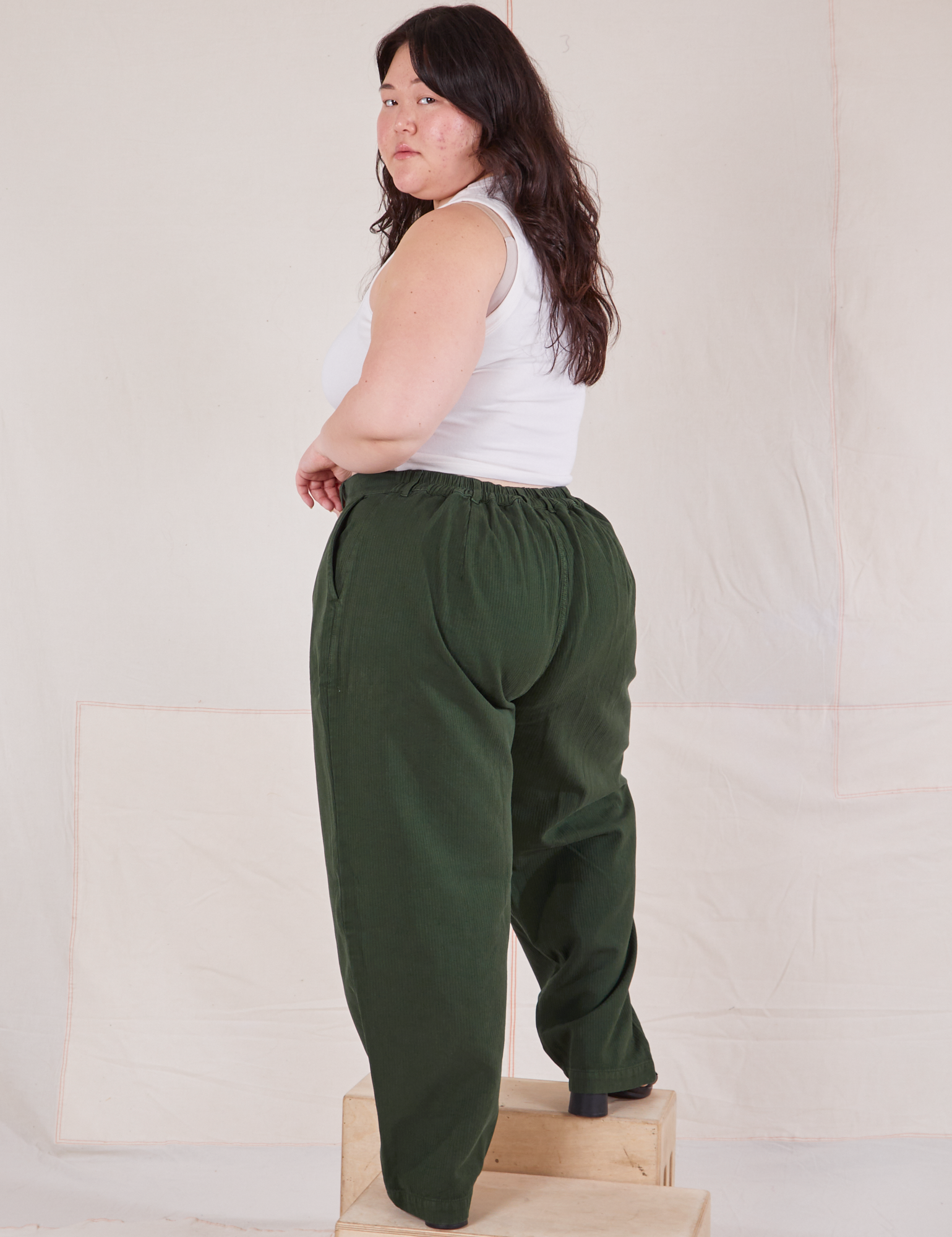 Angled back view of Heritage Trousers in Swamp Green and Cropped Tank Top in vintage tee off-white on Ashley