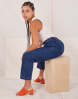 Gabi is sitting on a wooden crate facing the left. She is wearing Denim Trouser Jeans in Dark Wash and vintage off-white Tank Top