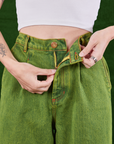 Overdyed Wide Leg Trousers in Gross Green front close up. Alex is pulling the zipper tab.