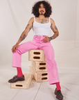 Jesse is sitting on a stack of wooden crates. They are wearing Carpenter Jeans in Bubblegum Pink and Cropped Cami in vintage tee off-white