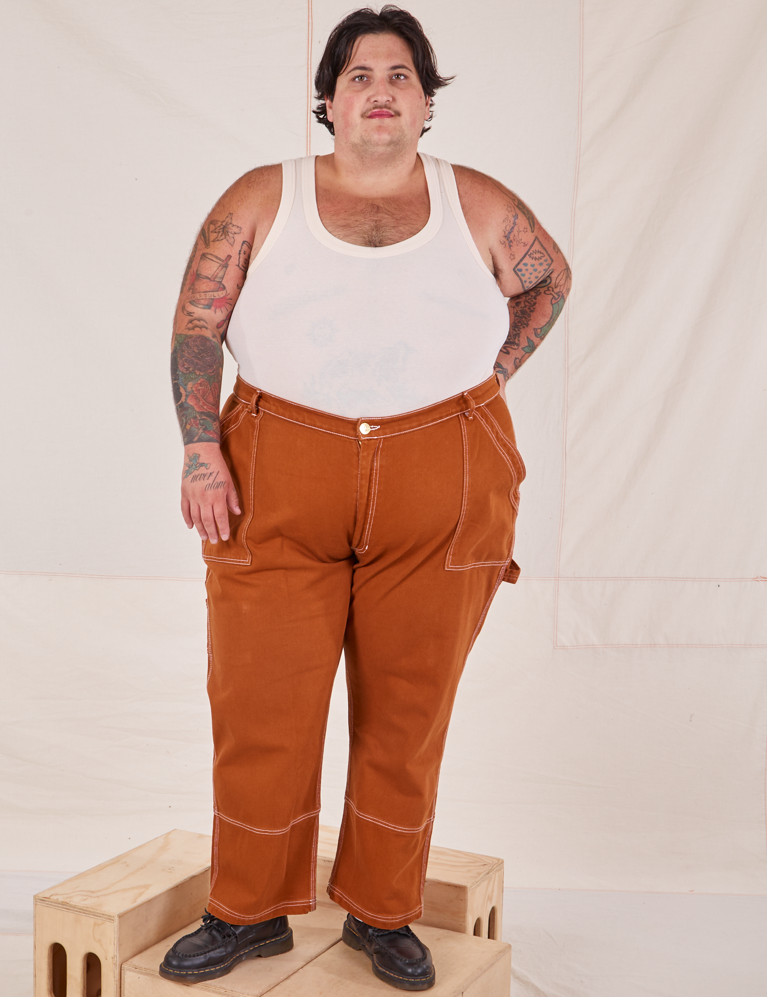 Sam is 5&#39;10&quot; and wearing 3XL Carpenter Jeans in Burnt Terracotta paired with Tank Top in vintage tee off-white