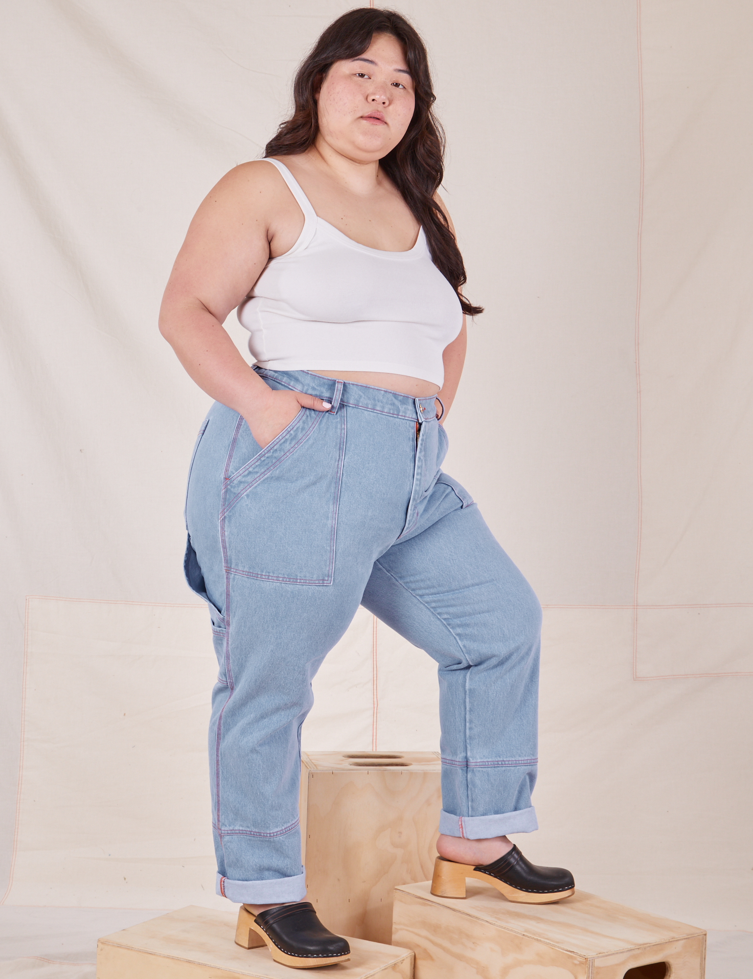 Angled front view of Carpenter Jeans in Light Wash and Cropped Cami in vintage tee off-white worn by Ashley