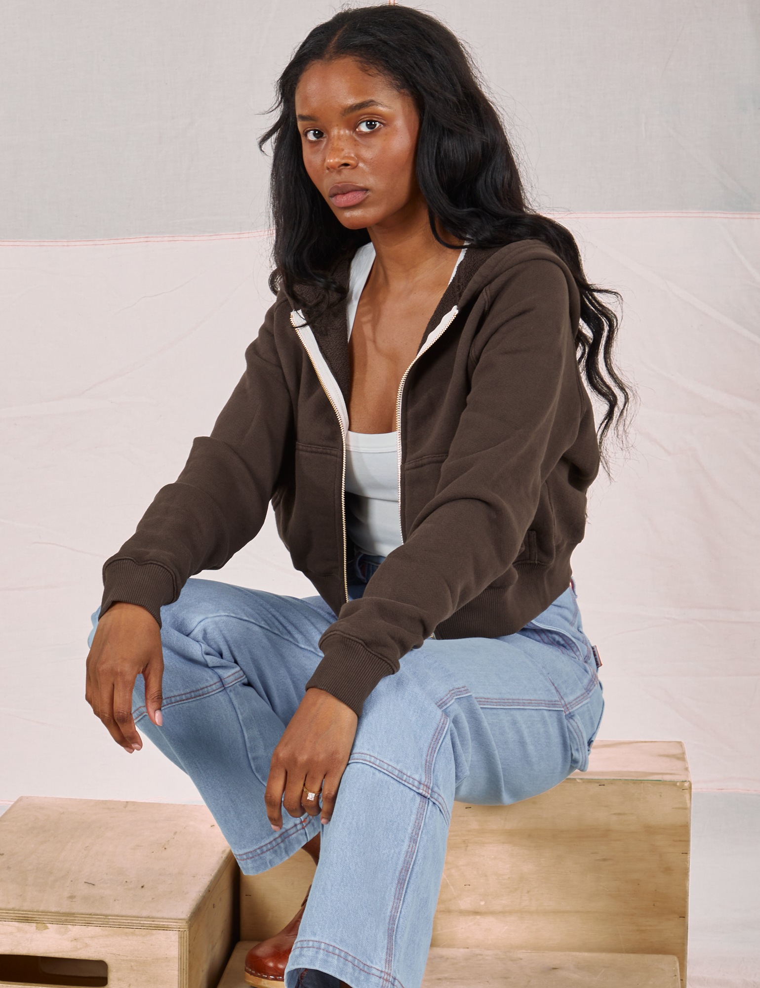 Kandia is wearing Cropped Zip Hoodie in Espresso Brown and light wash Carpenter Jeans