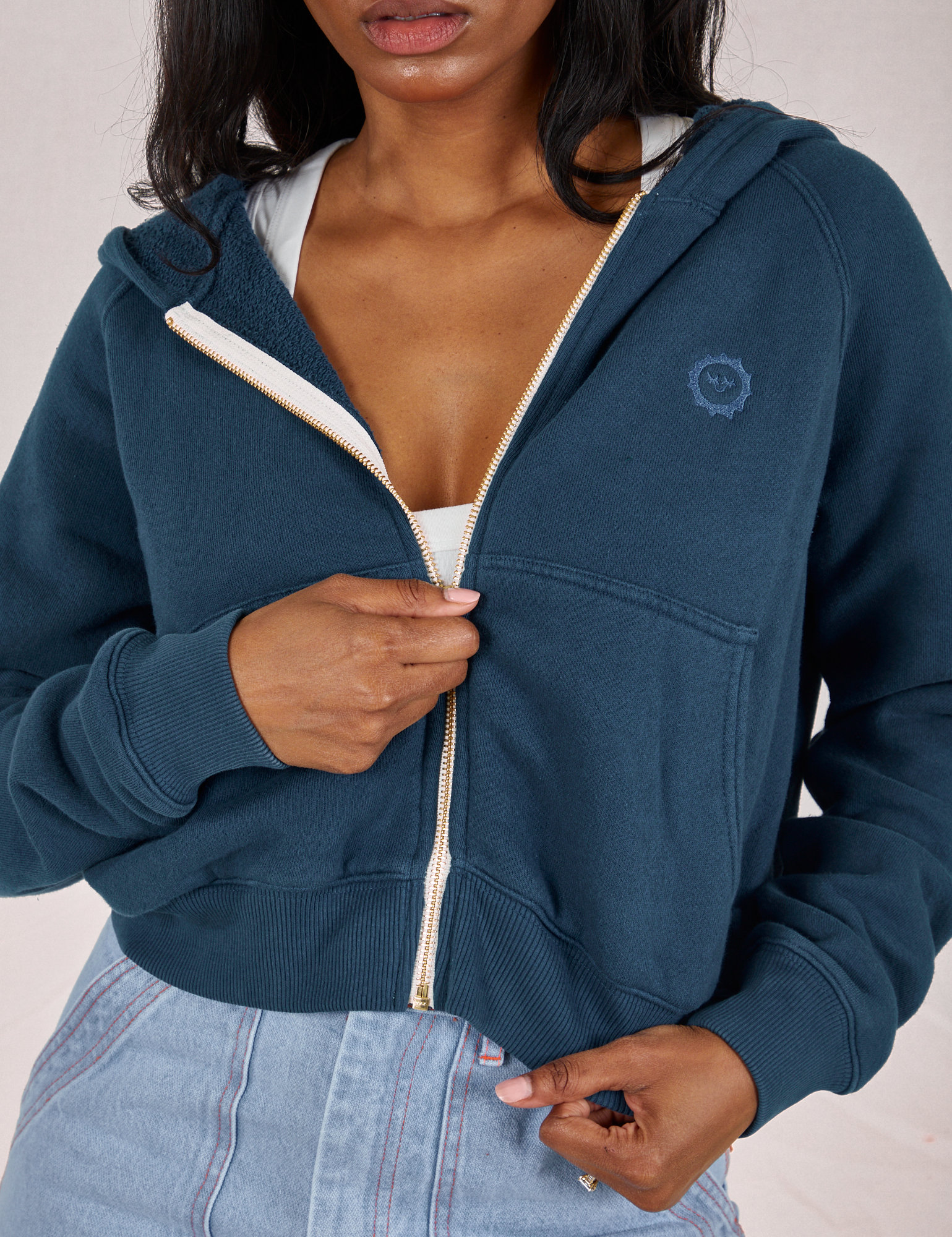 Front close up of Cropped Zip Hoodie in Lagoon. Kandia is pulling on the zipper tab.