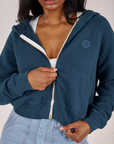 Front close up of Cropped Zip Hoodie in Lagoon. Kandia is pulling on the zipper tab.