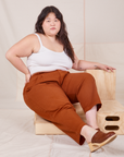 Ashley is sitting on a wooden crate. She is wearing Heavyweight Trousers in Burnt Terracotta and Cropped Cami in vintage tee off-white