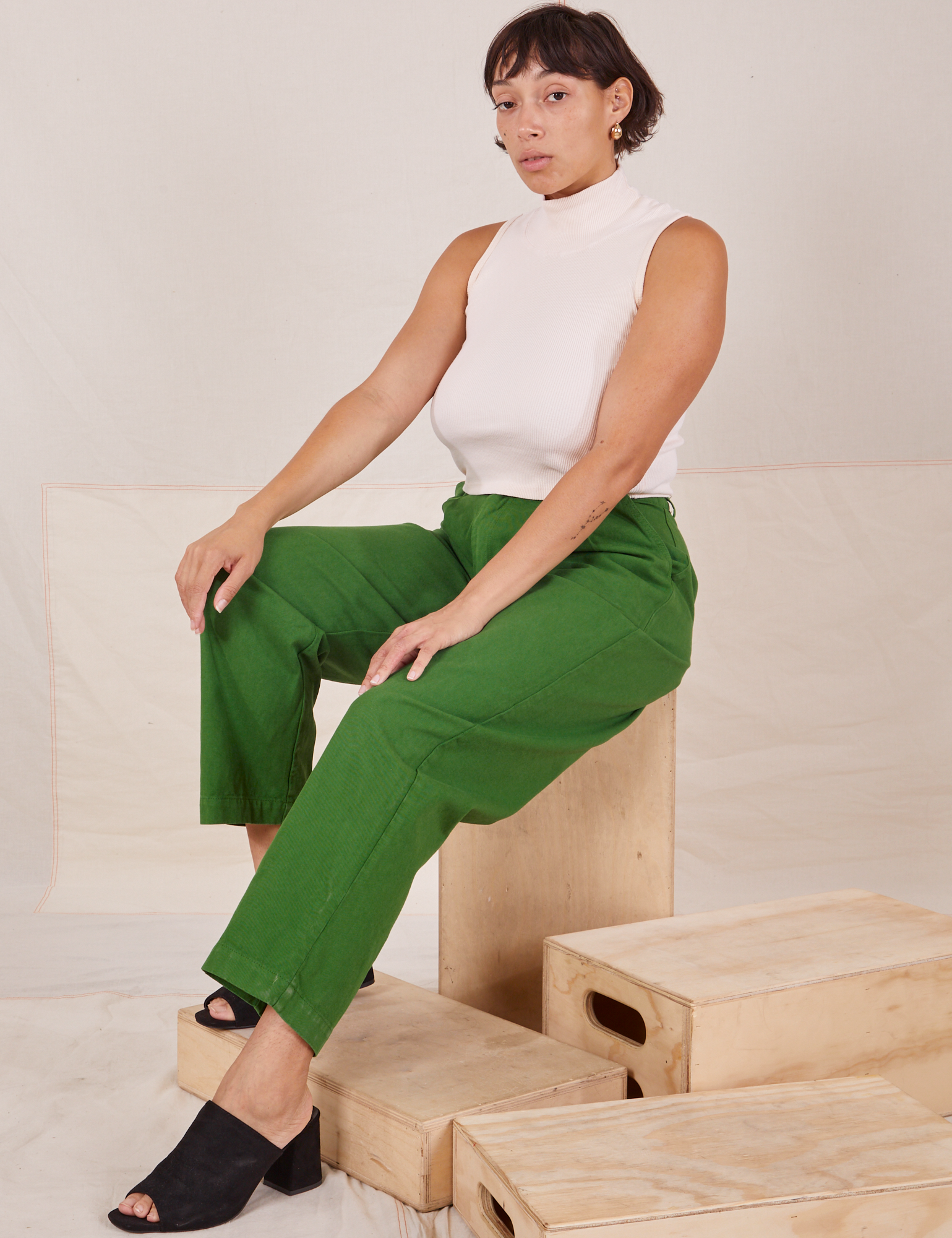Tiara is sitting on a wooden crate. She is wearing Heavyweight Trousers in Lawn Green and Sleeveless Turtleneck in vintage tee off-white