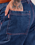 Carpenter Shorts in Dark Wash back pocket close up. Jesse has their hand in the pocket.