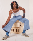 Jerrod is sitting on a stack of crates. They are wearing Indigo Wide Leg Trousers in Light Wash and vintage off-white Cami