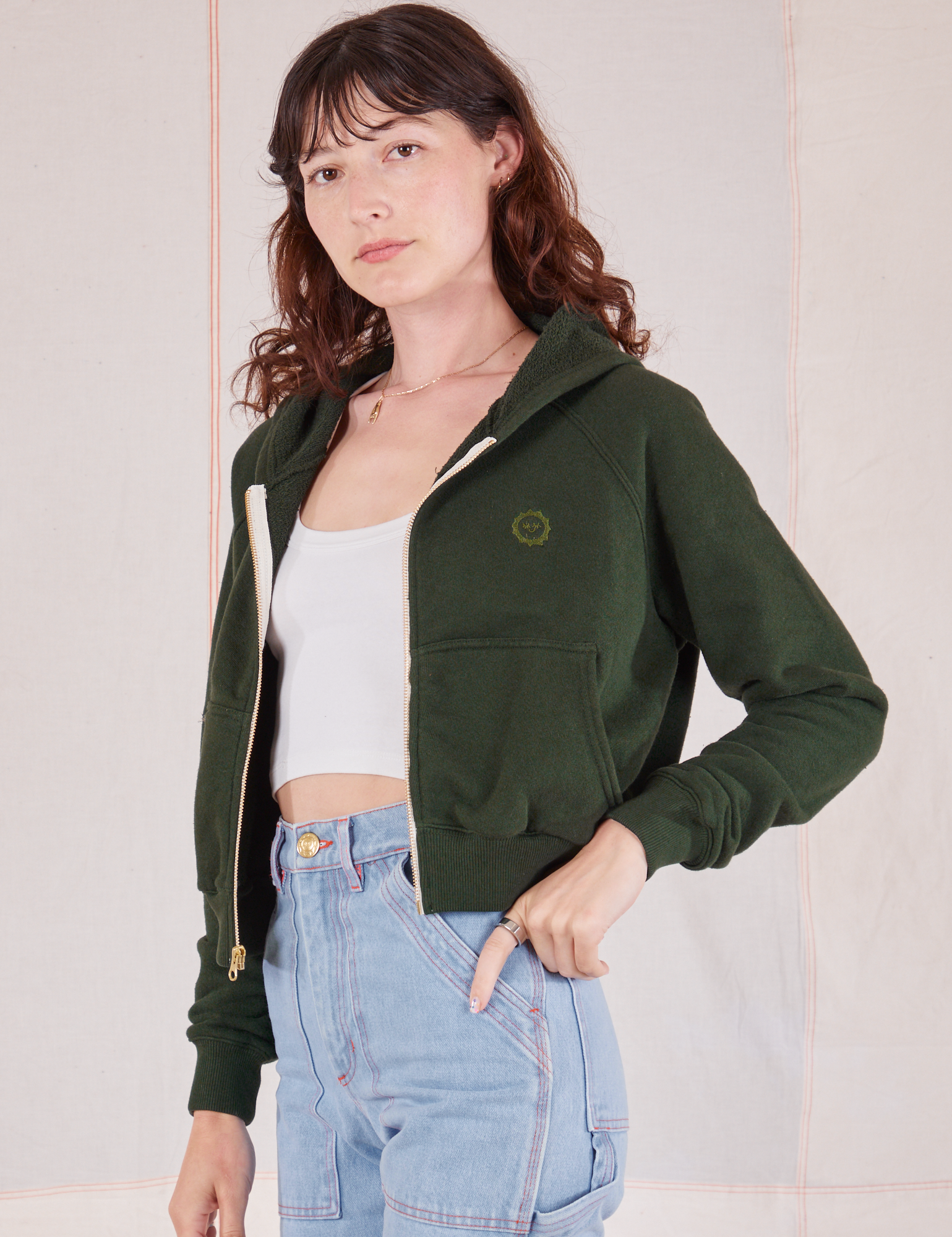 Angled front view of Cropped Zip Hoodie in Swamp Green, vintage off-white Cropped Tank and light wash Carpenter Jeans
