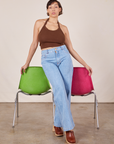 Tiara is standing in front of a green and pink chair with her hands resting on each. She is wearing Halter Top in Fudgesicle Brown and light wash Sailor Jeans.