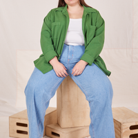 Marielena is sitting on a wooden crate wearing Oversize Overshirt in Lawn Green paired with vintage off-white Cropped Tank Top and light wash Sailor Jeans