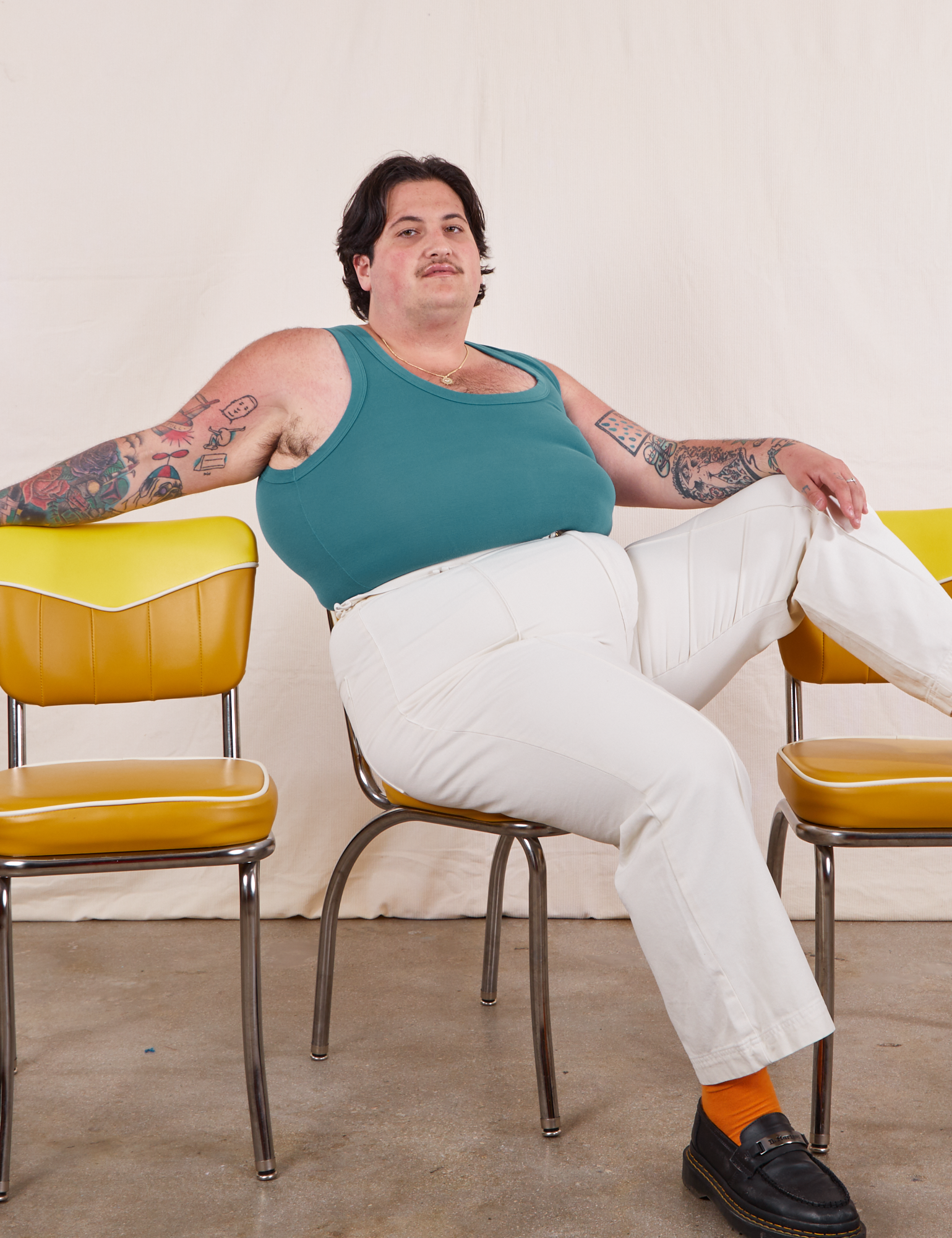 Sam is sitting on a yellow chair wearing Tank Top in Marine Blue and vintage tee off-white Western Pants