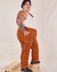 Side view of Carpenter Jeans in Burnt Terracotta and Tank Top in vintage tee off-white on Sam