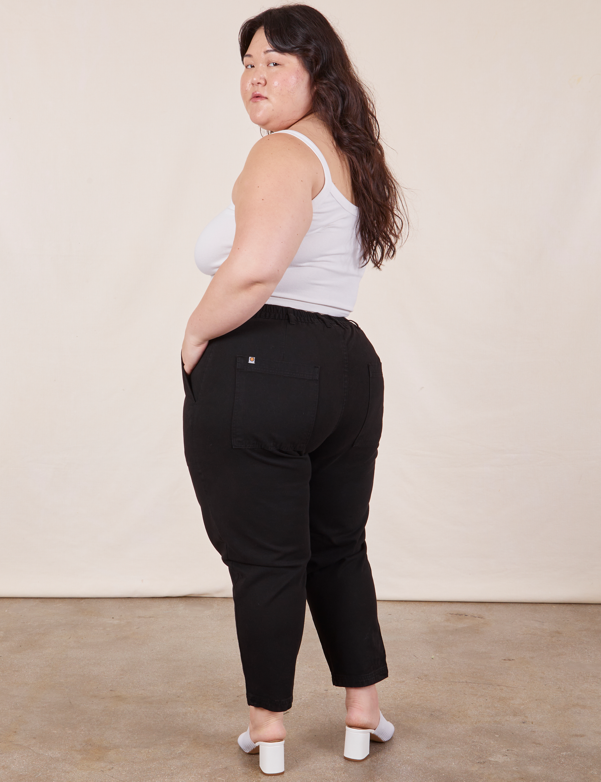 Angled back view of Petite Pencil Pants in Basic Black and Cropped Cami In vintage tee off-white worn by Ashley
