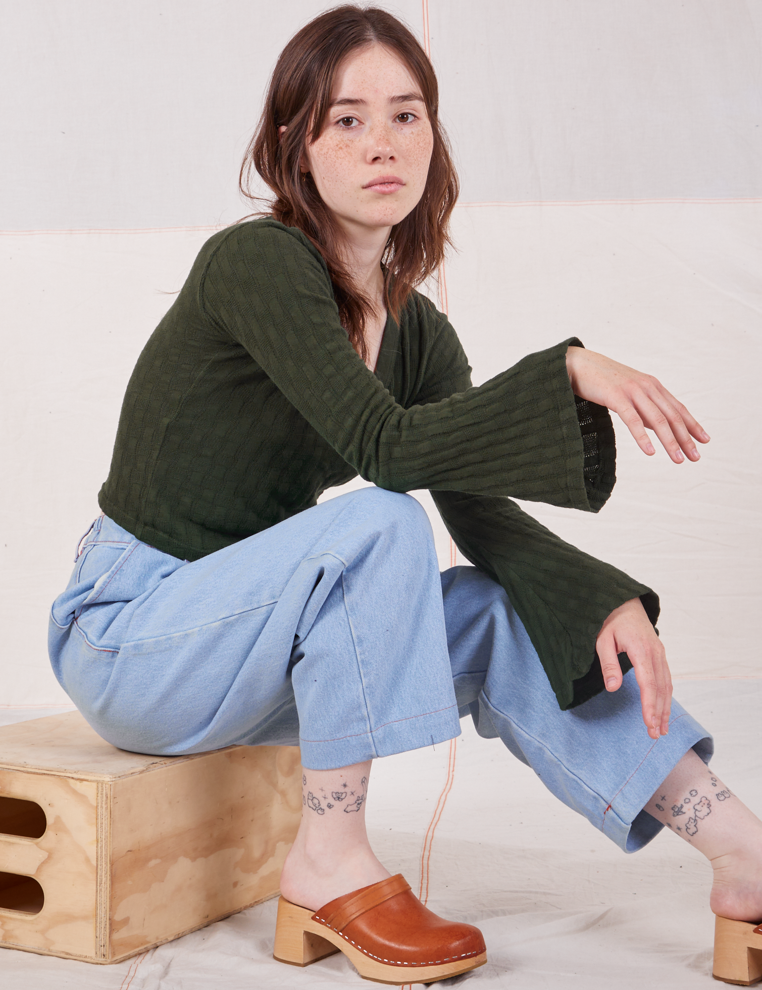 Hana is wearing Bell Sleeve Top in Swamp Green and light wash Petite Trouser Jeans
