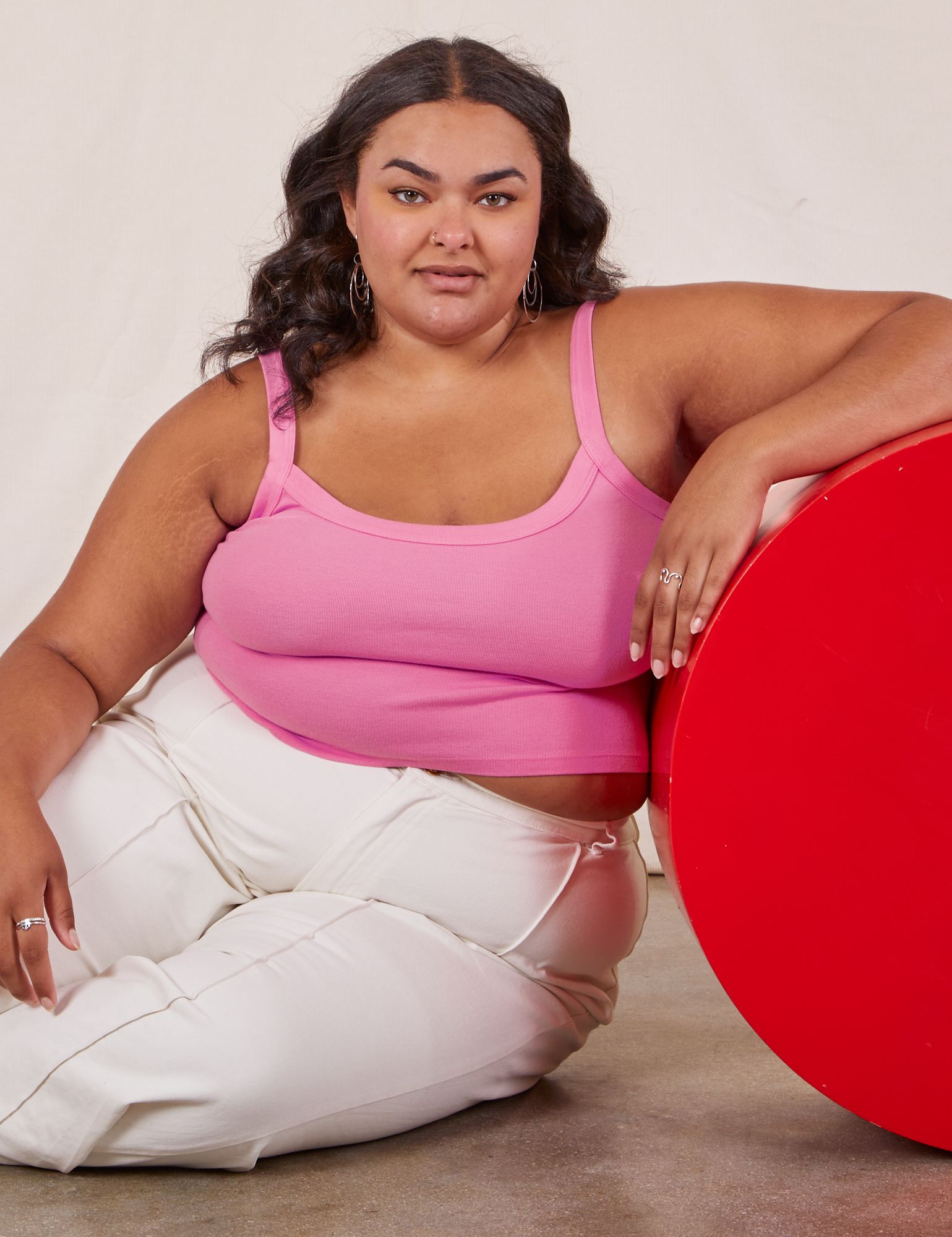 Alicia is sitting on the floor and has her right elbow on a red circular platform. She is wearing Cropped Cami in Bubblegum Pink and vintage tee off-white Western Pants.