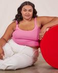 Alicia is sitting on the floor and has her right elbow on a red circular platform. She is wearing Cropped Cami in Bubblegum Pink and vintage tee off-white Western Pants.