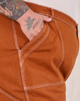 Carpenter Jeans in Burnt Terracotta front pocket close up. Sam has their hand in the pocket.