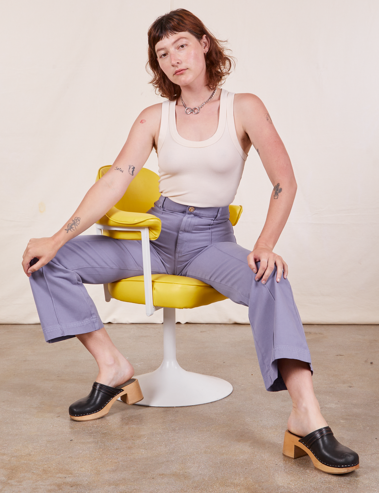 Alex is sitting in a yellow and white chair wearing Western Pants in Faded Grape and a Tank Top in vintage tee off-white