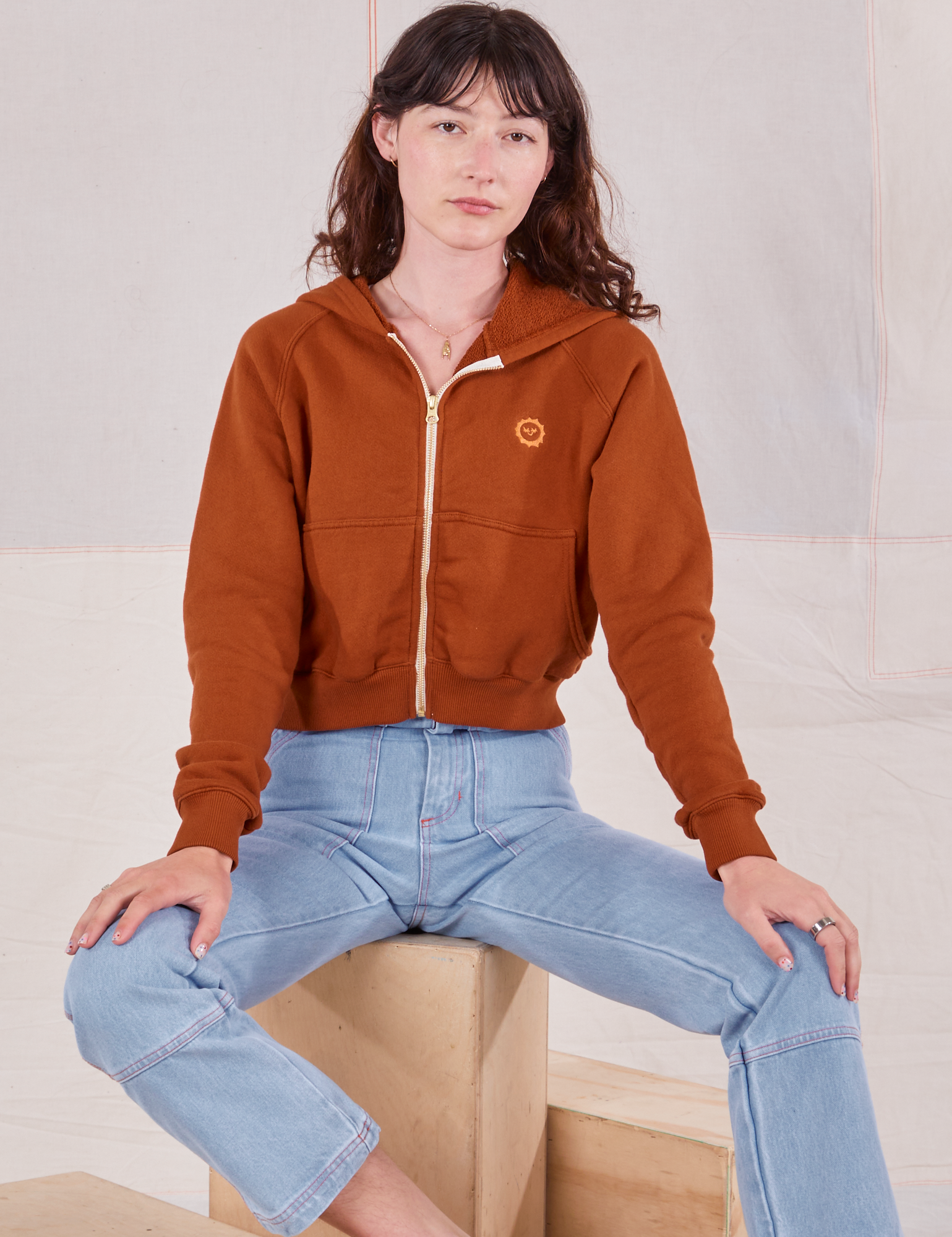 Alex is wearing Cropped Zip Hoodie in Burnt Terracotta and light wash Carpenter Jeans