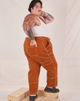 Angled back view of Carpenter Jeans in Burnt Terracotta and Tank Top in vintage tee off-white on Sam