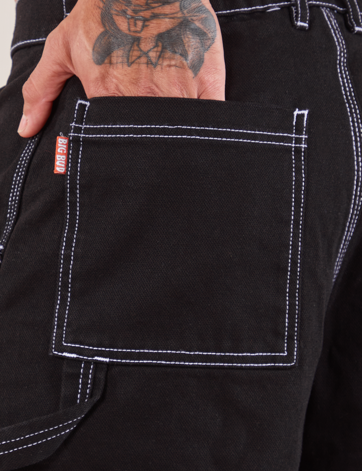 Carpenter Shorts in Basic Black back pocket close up. Jesse has their hand in the pocket.