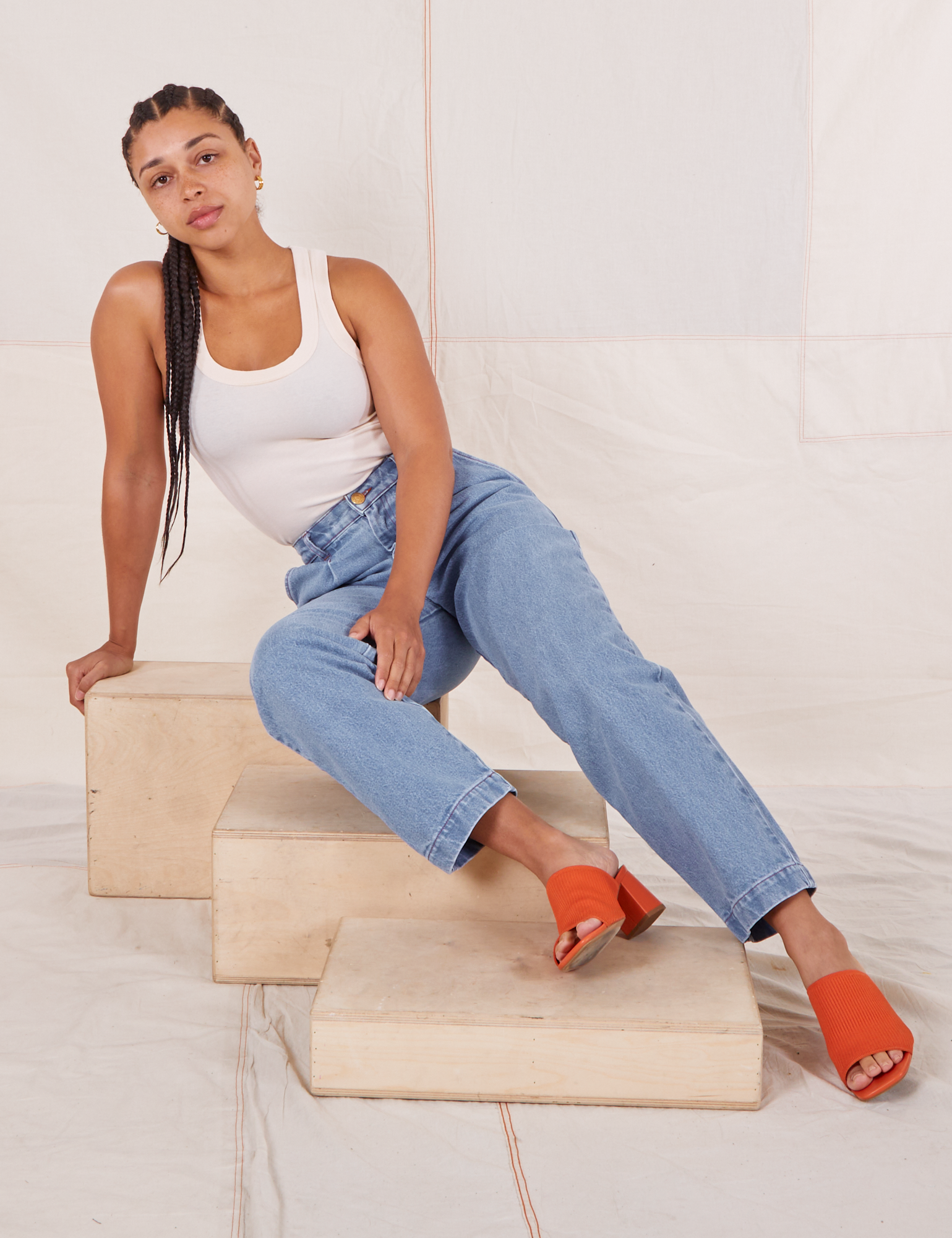 Gabi is sitting on a wooden crate wearing Denim Trouser Jeans in Light Wash and Tank Top in vintage tee off-white
