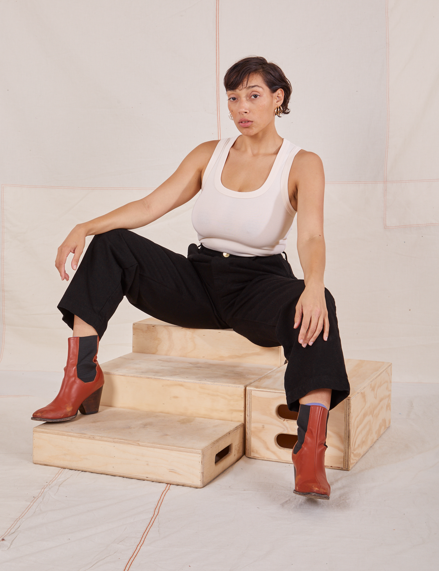 Tiara is sitting on a wooden crate wearing Denim Trouser Jeans in Black and Tank Top in vintage tee off-white