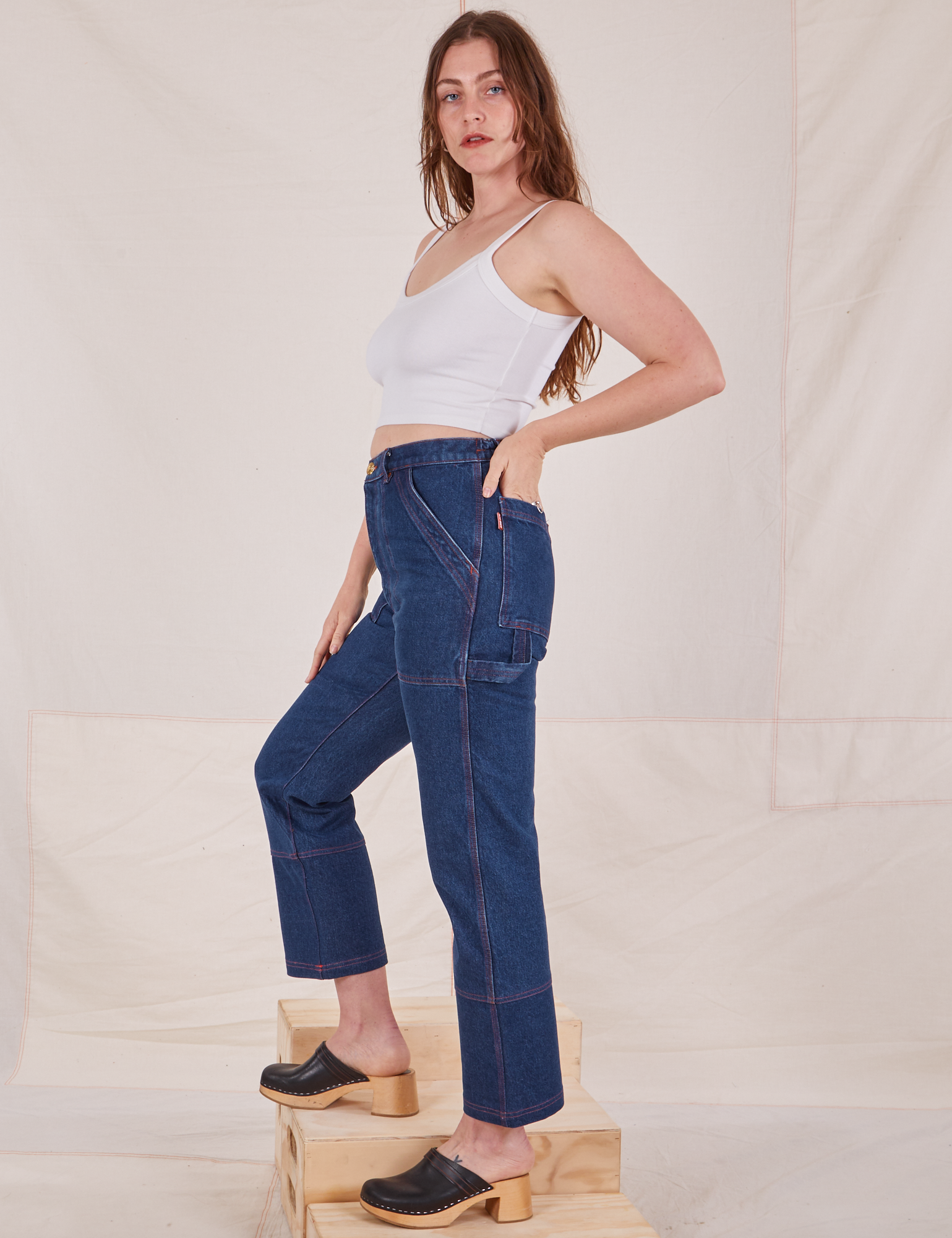 Side view of Carpenter Jeans in Dark Wash and Cropped Cami in vintage tee off-white worn by Allison