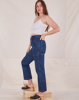 Side view of Carpenter Jeans in Dark Wash and Cropped Cami in vintage tee off-white worn by Allison