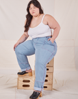 Ashley is sitting on a stack of wooden crates wearing Carpenter Jeans in Light Wash