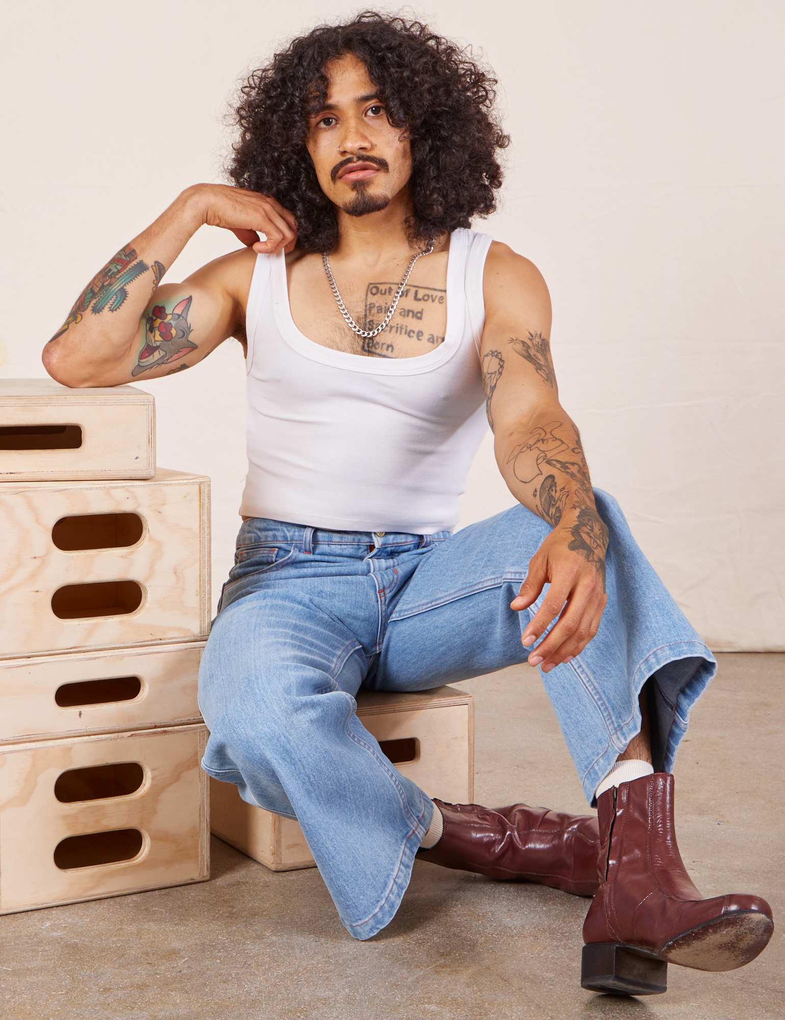 Jesse is wearing Cropped Tank Top in Vintage Tee Off-White and sitting on a wooden crate